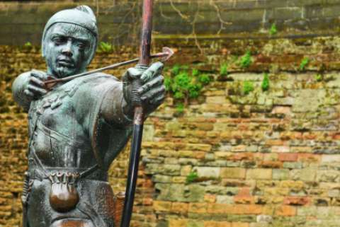 A brass statue of a medieval archer resembling Robin Hood is in front of a dilapidated brick wall