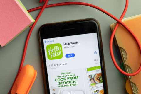An iPhone sits on a mess desk displaying the HelloFresh page in the App Store