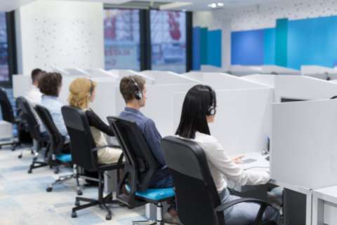 Call center operators sitting in their cubicles, wearing headsets, depicted from behind