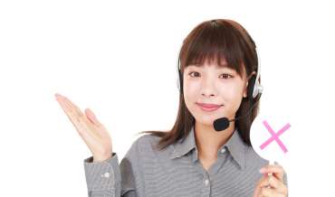 A woman with a headset telephone raises her right palm and holds a sign with a red X in her left hand