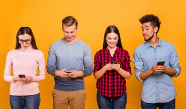 4 people stand in front of an orange wall, looking at their smartphones