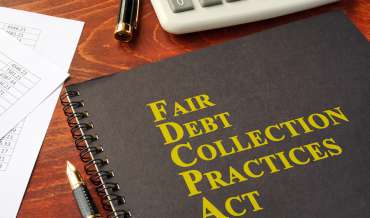 A notebook that reads "Fair Debt Collection Practices Act" sits on a wooden desk next to pens and a calculator