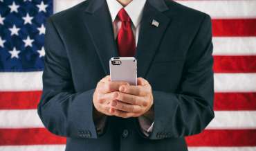 a man in a business suit sends a text message while standing in front of the American flag