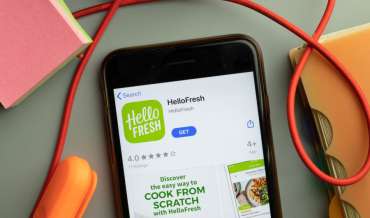 An iPhone sits on a mess desk displaying the HelloFresh page in the App Store