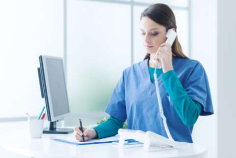 A nurse in a hosital is answering a phone and taking notes