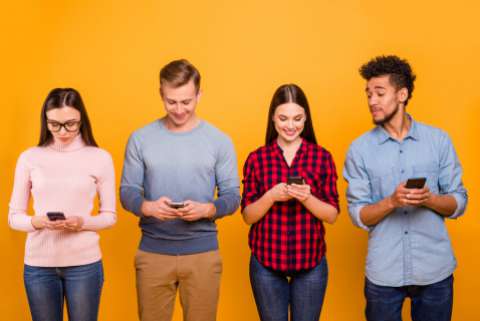 4 people stand in front of an orange wall, looking at their smartphones
