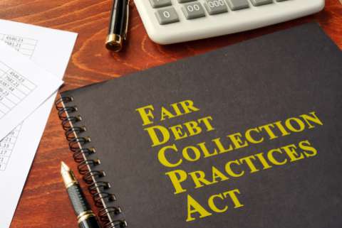A notebook that reads "Fair Debt Collection Practices Act" sits on a wooden desk next to pens and a calculator
