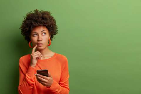 a woman holds a phone and ponders something in front of a green background