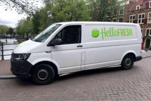 A HelloFresh van is parked on a bridge over a river in a city.