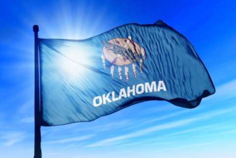 Oklahoma flag waving with the sun and blue sky behind it