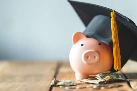 A piggy bank wearing a graduation cap with crumpled dollar bills in front of it