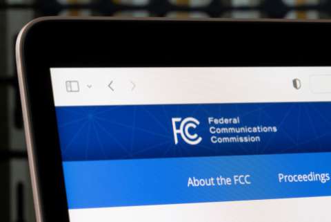 The top left corner of a laptop screen displays part of the header for the FCC's website