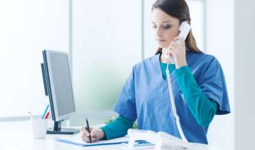 A nurse in a hosital is answering a phone and taking notes