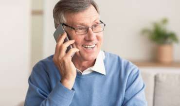 Elderly Man Talking On Cellphone Sitting On Couch At Home