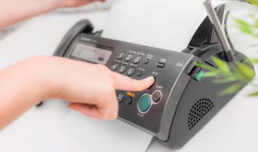 A finger presses the stop button on a fax machine