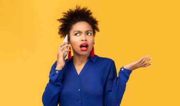 A woman in front of an orange background answers her phone and is annoyed