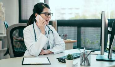 A doctor sits at her desk and has a conversation on a cell phone