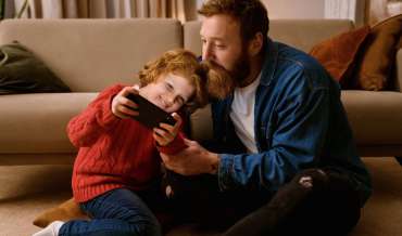 Father and son playing online game on mobile phone together while sitting on floor