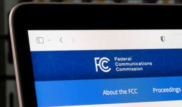The top left corner of a laptop screen displays part of the header for the FCC's website